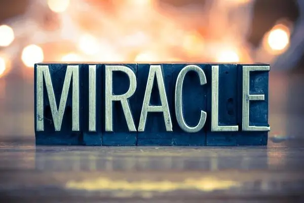 the word miracle in old type blocks on a table with lights behind it.